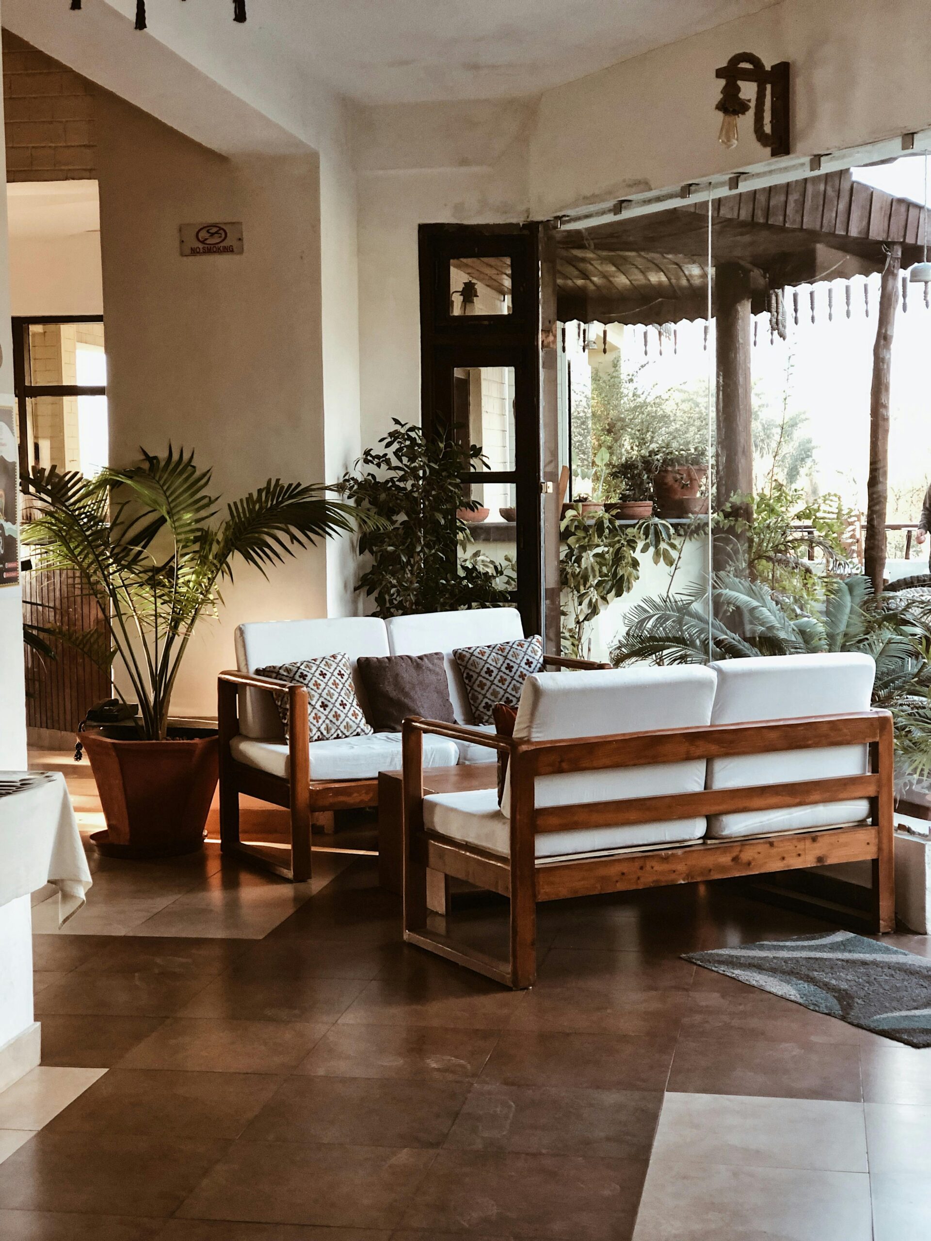 Warm and inviting living room featuring wooden furniture, indoor plants, and large glass windows overlooking nature.